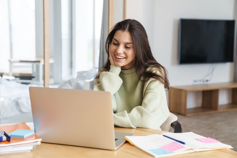Cheerful College Student Using Laptop While Doing Homework