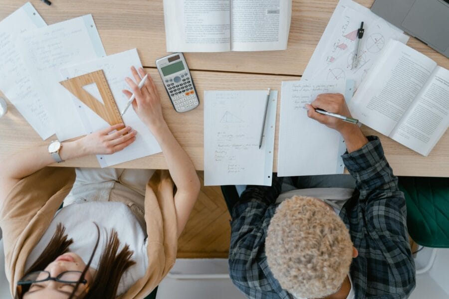 Overhead view of two students studying math with books, calculator, and geometry tools.