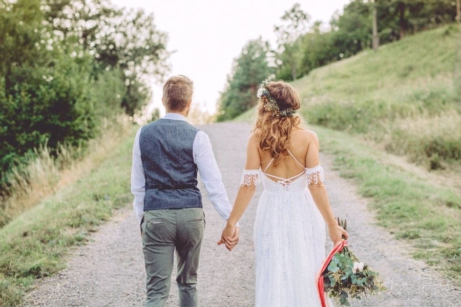bride carrying bouquet at her side with groom holding her hand on the other walking up gravel road