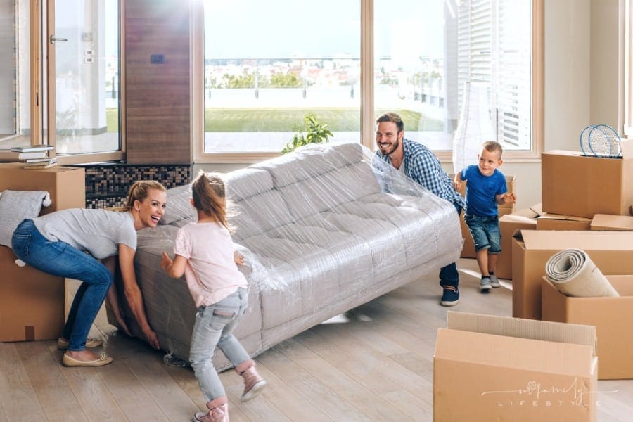 young parents carrying sofa into new house with kids running around them