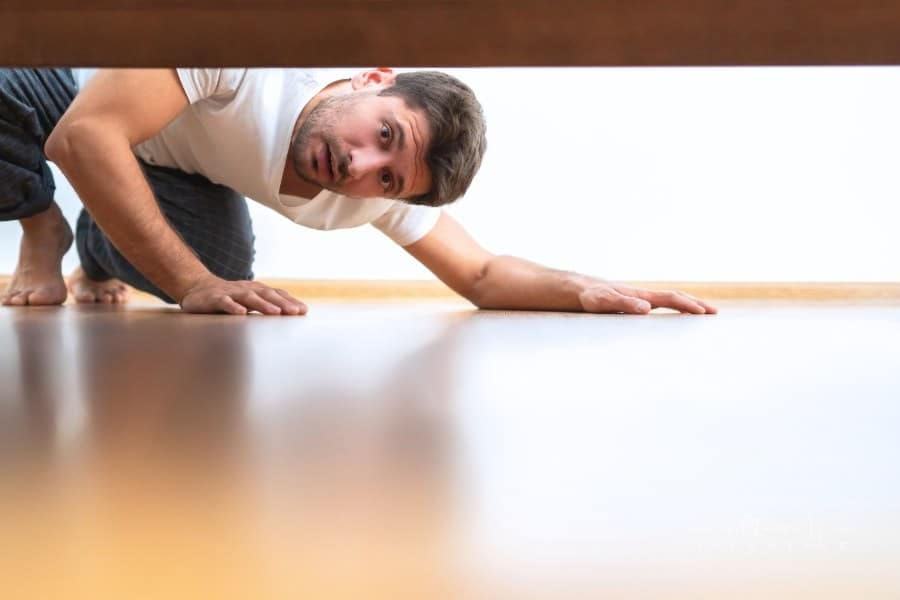 man looking under the bed for lost item