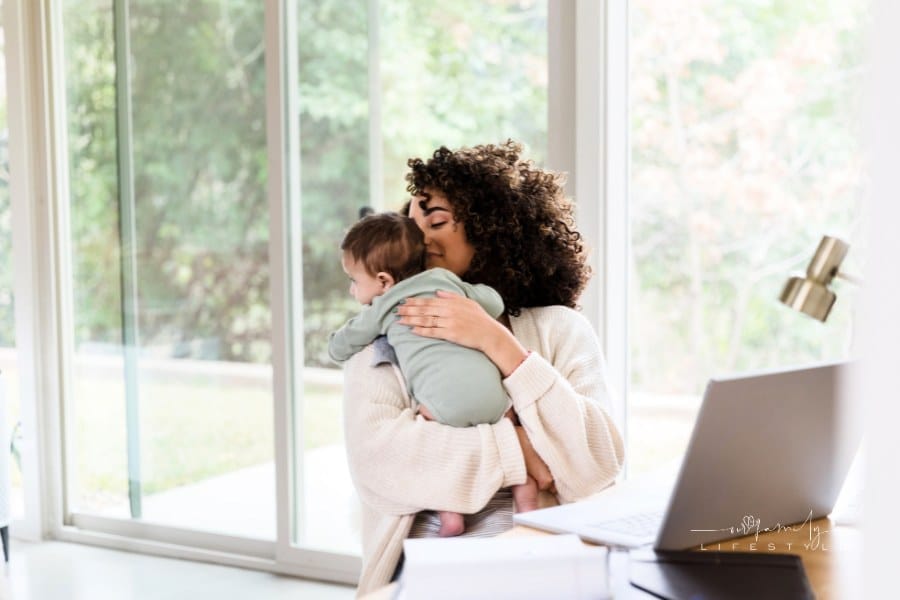 Mom multi-tasks on laptop while caring for newborn baby