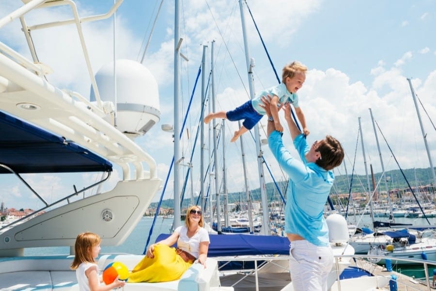 dad lifting laughing toddler on yacht while mom and sister look on
