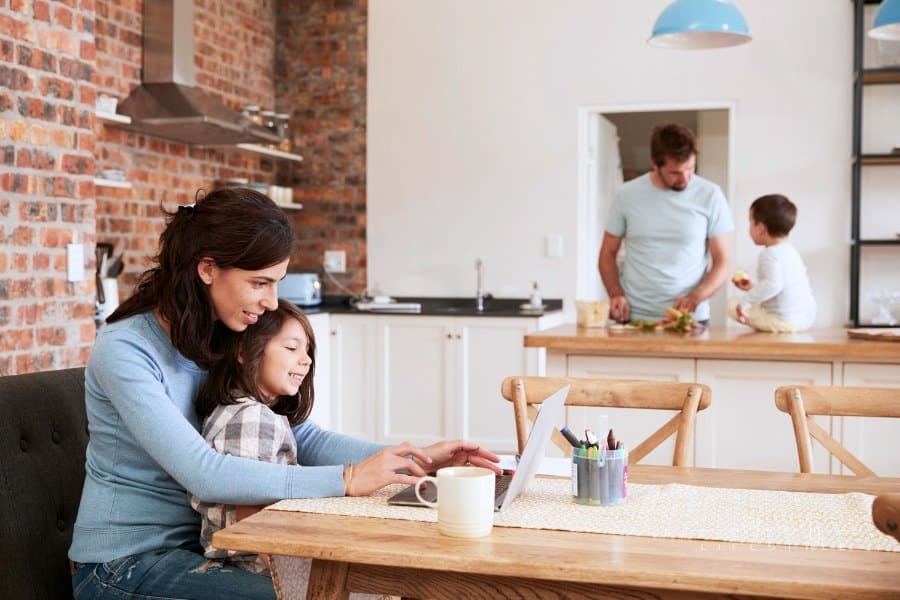 Busy Family Home With Mother Working As Father Prepares Meal