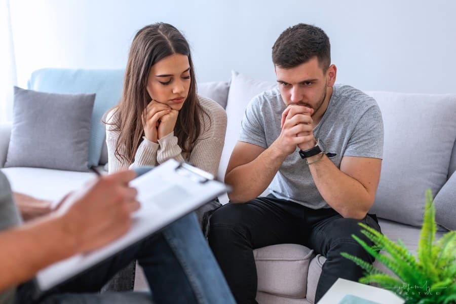 Sad marriage talking with female therapist, horizontal. Married couple during psychotherapy and psychologist back view. Young