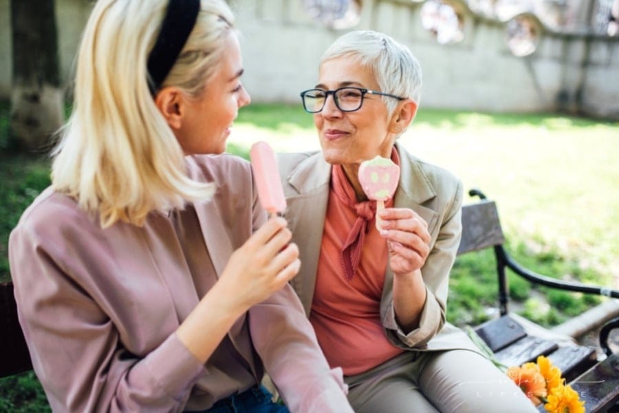 adult daughter enjoying ice cream with mature mom on a park bench