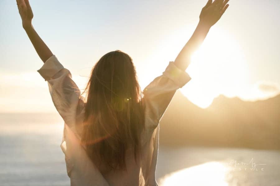 Happy woman open arms at mountain peak cliff.