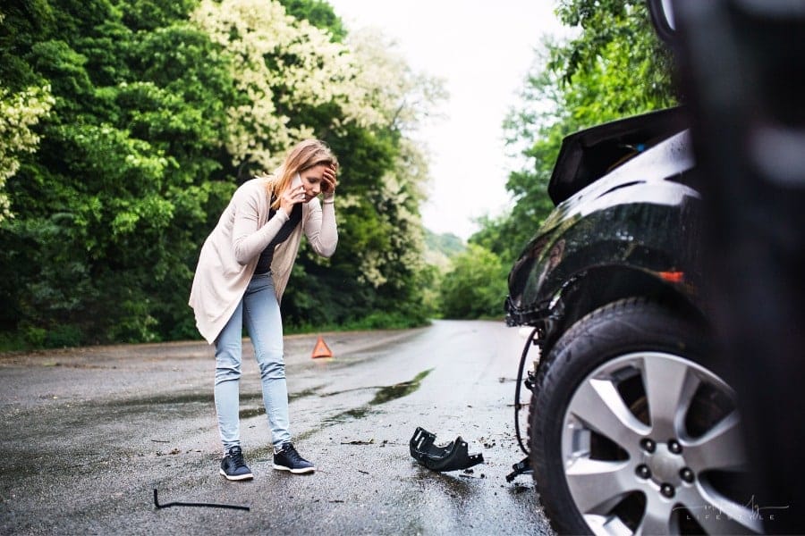 frustrated woman talking on phone by damaged car after accident