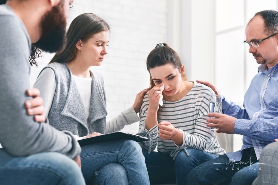 Therapy crisis. Understanding people calming depressed crying woman during group session meeting in rehab, giving her glass o