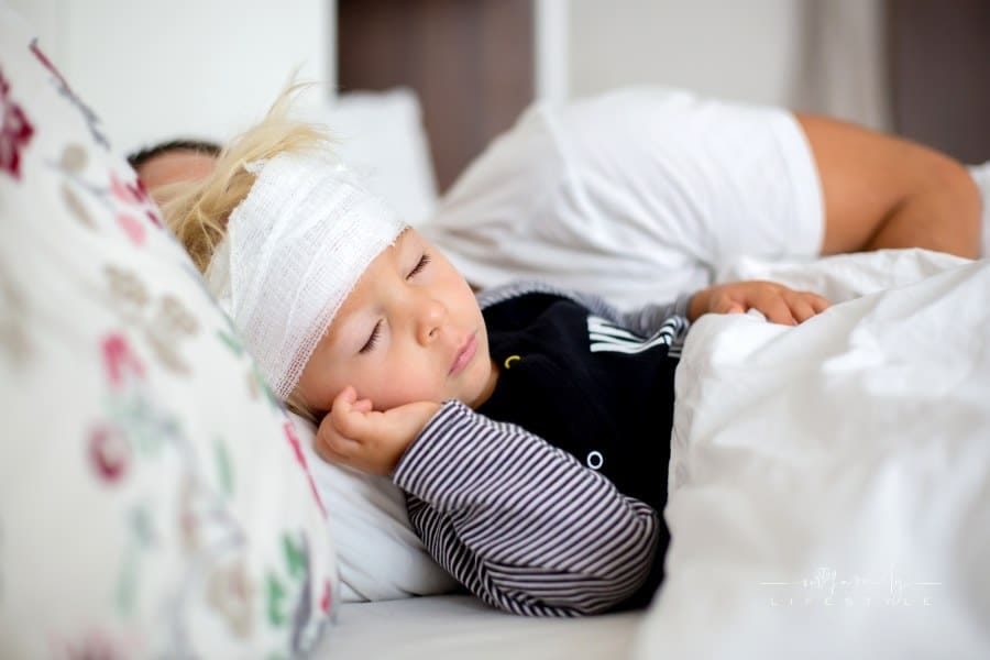 Little toddler boy with head injury, lying in bed, tired, sleeping