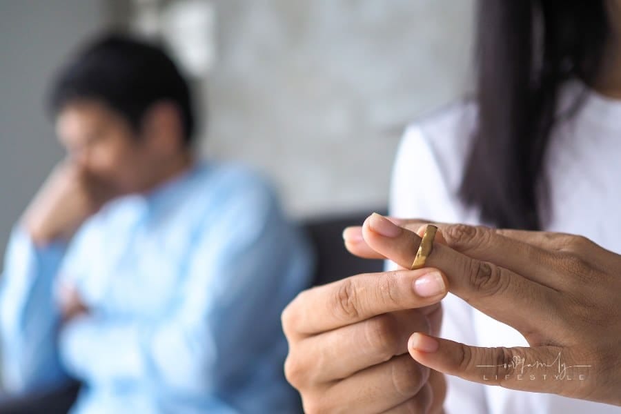 Woman Taking Wedding Ring Off with Husband behind her
