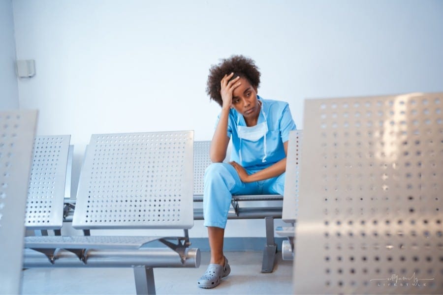 tired nurse sitting in waiting room chair with hand on head
