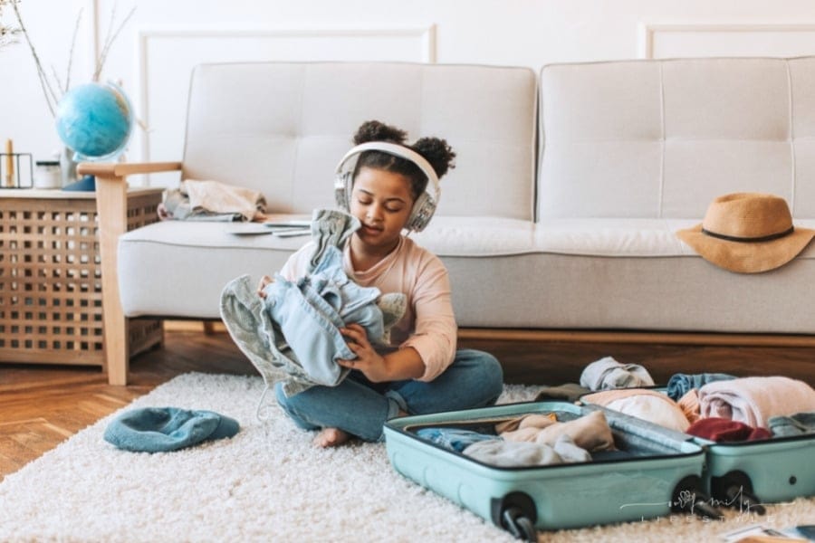 young girl with headphones packing suitcase