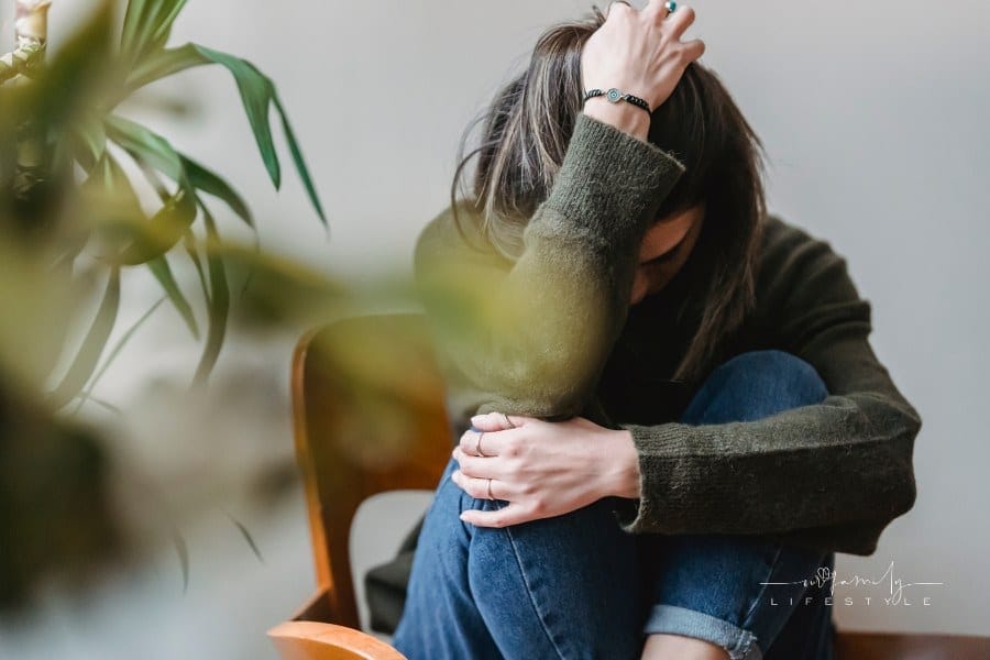Unrecognizable upset woman embracing knees sitting on chair