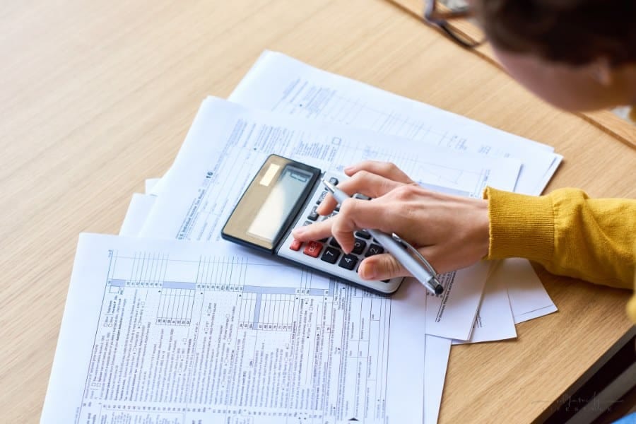 Close-up of busy woman sitting at wooden coffee table and calculating tax figures while examining tax returns papers