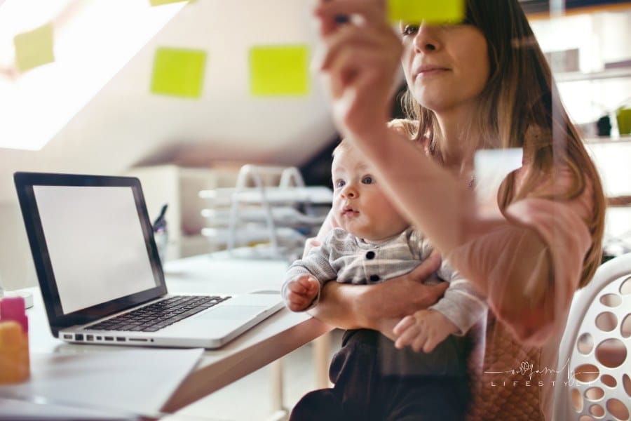mom working while holding baby and adding sticky notes to wall