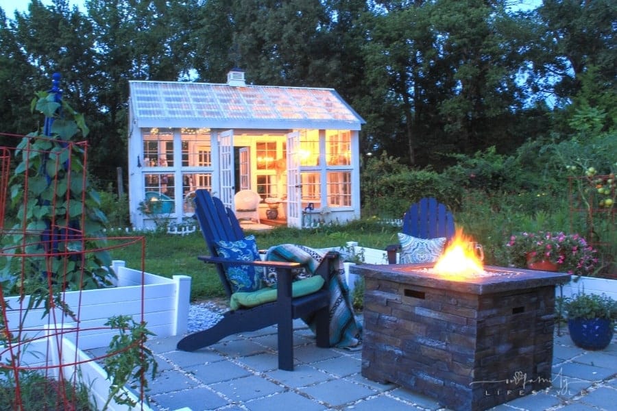 backyard fire pit surrounded by patio chairs with greenhouse in background