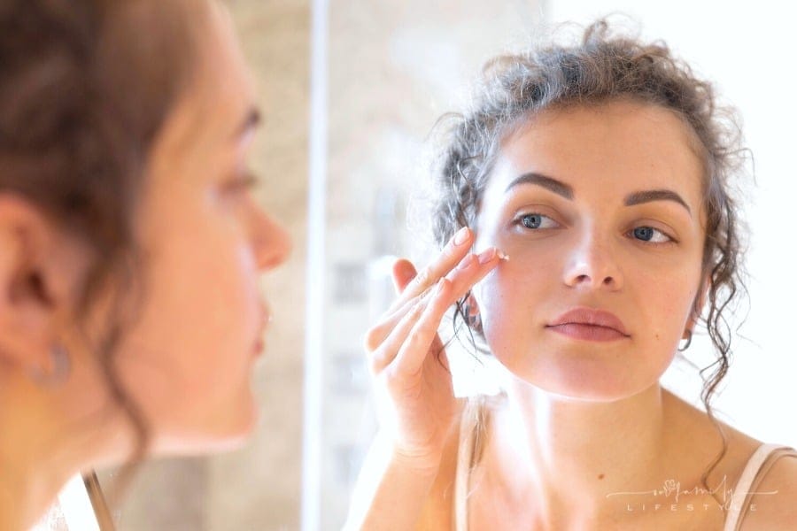 woman looking into mirror applying face cream