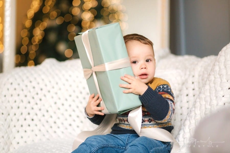 toddler boy in sweater hugging wrapped gift on couch